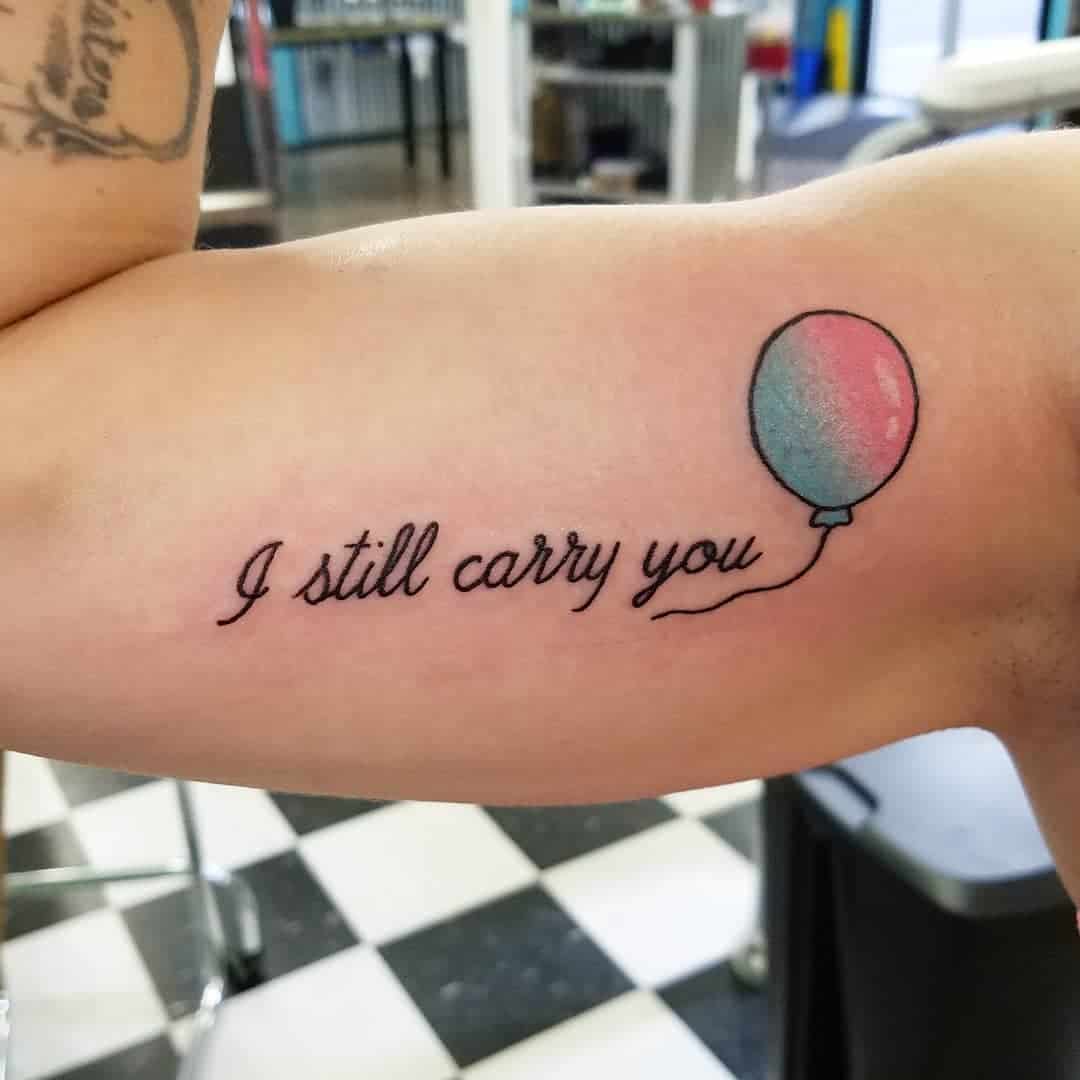 A tattoo of a balloon with the text "I still carry you" on an arm