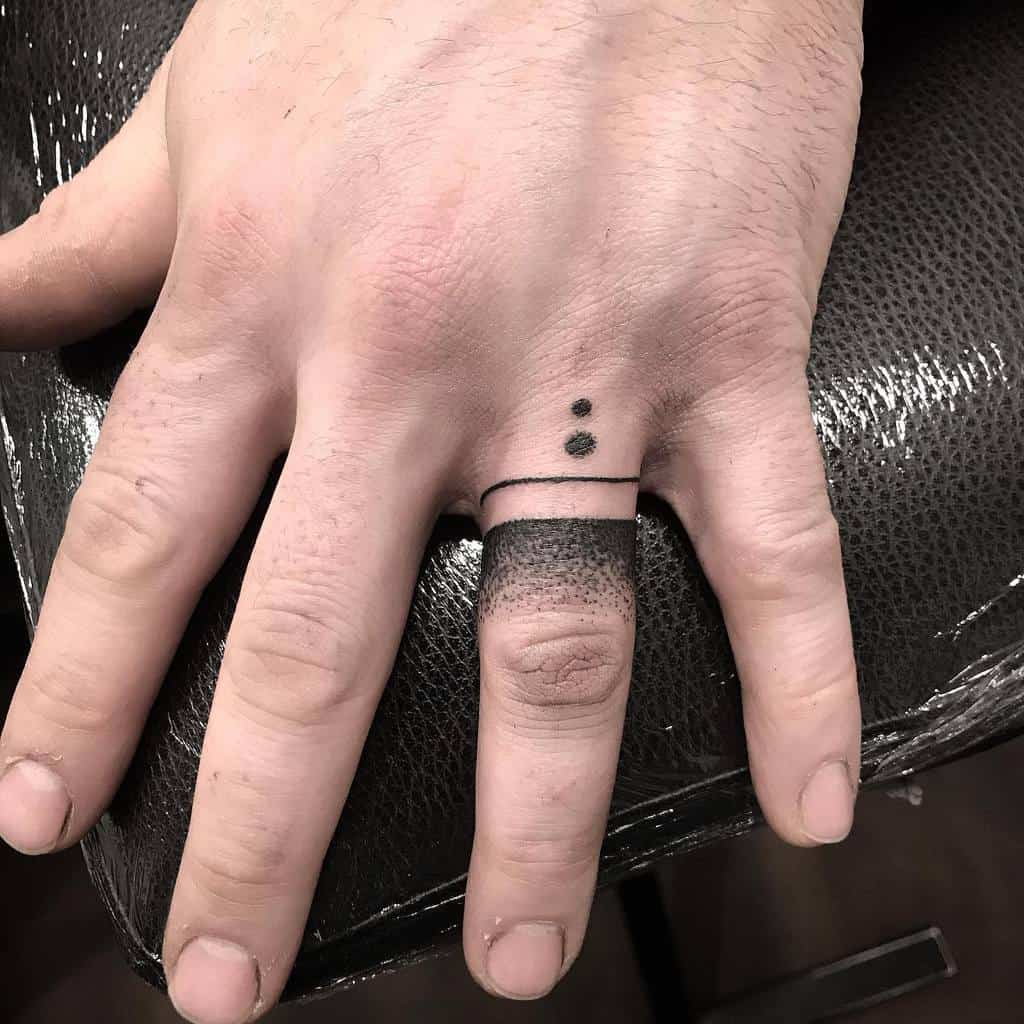 A black band ring tattoo with two small black dots above it