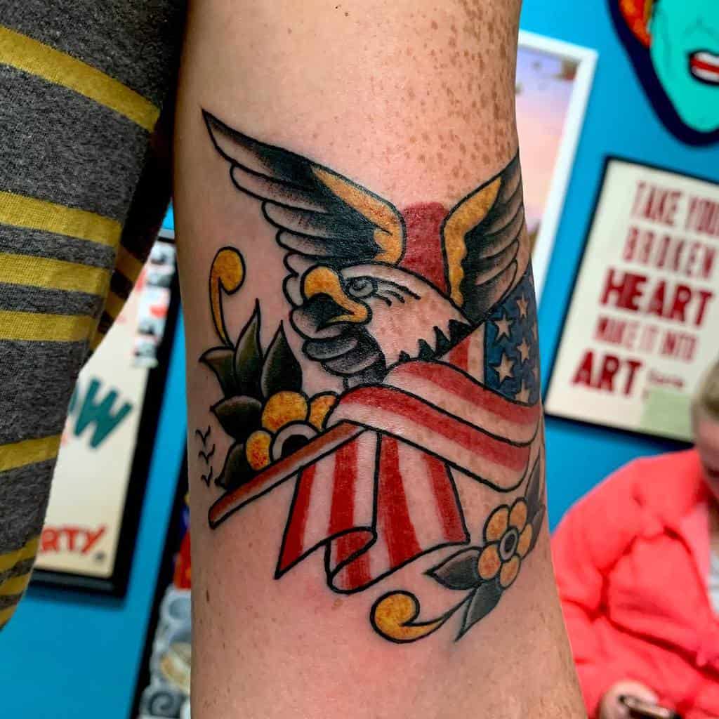 Tattoo of an eagle with U.S. flag wings and flowers on an arm