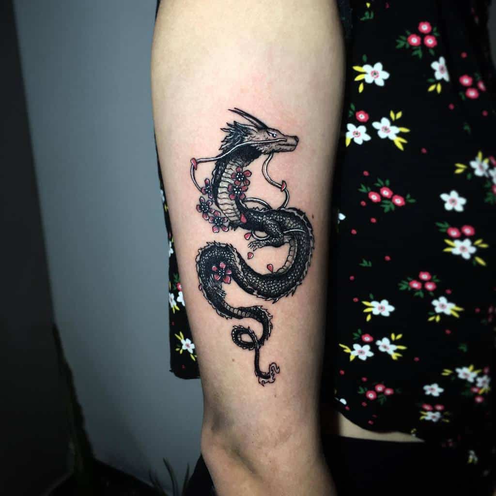 Tattoo of a dragon with red flowers on an upper arm