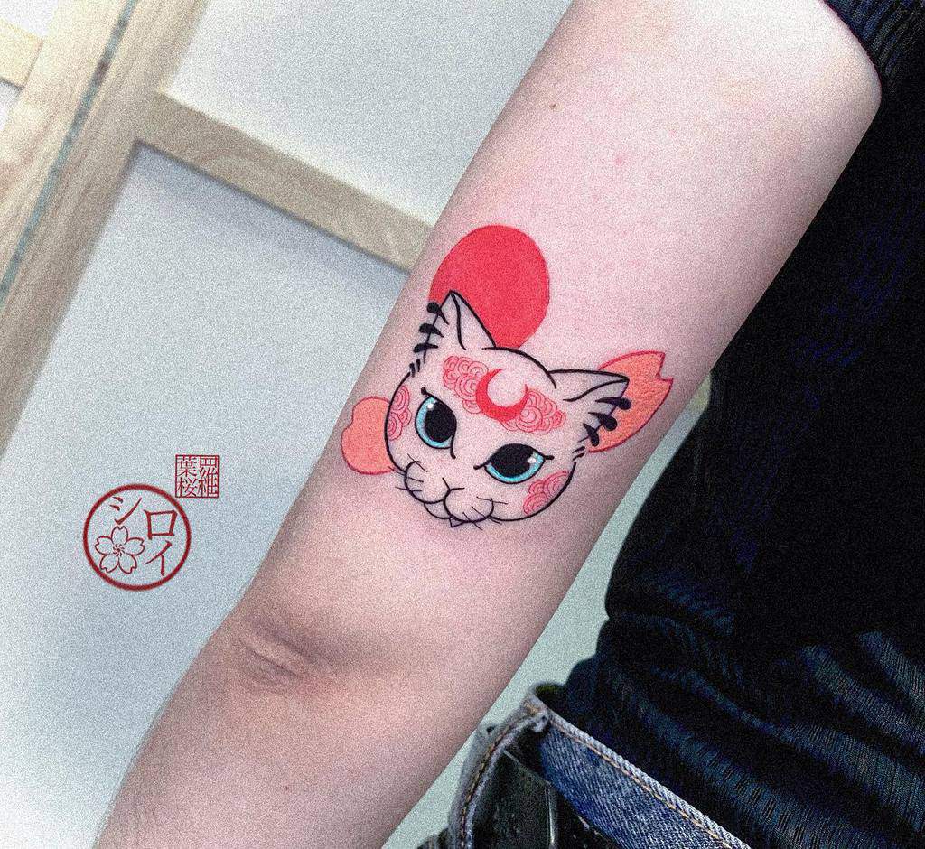 Tattoo of a stylized cat with pink and red accents on a woman's arm