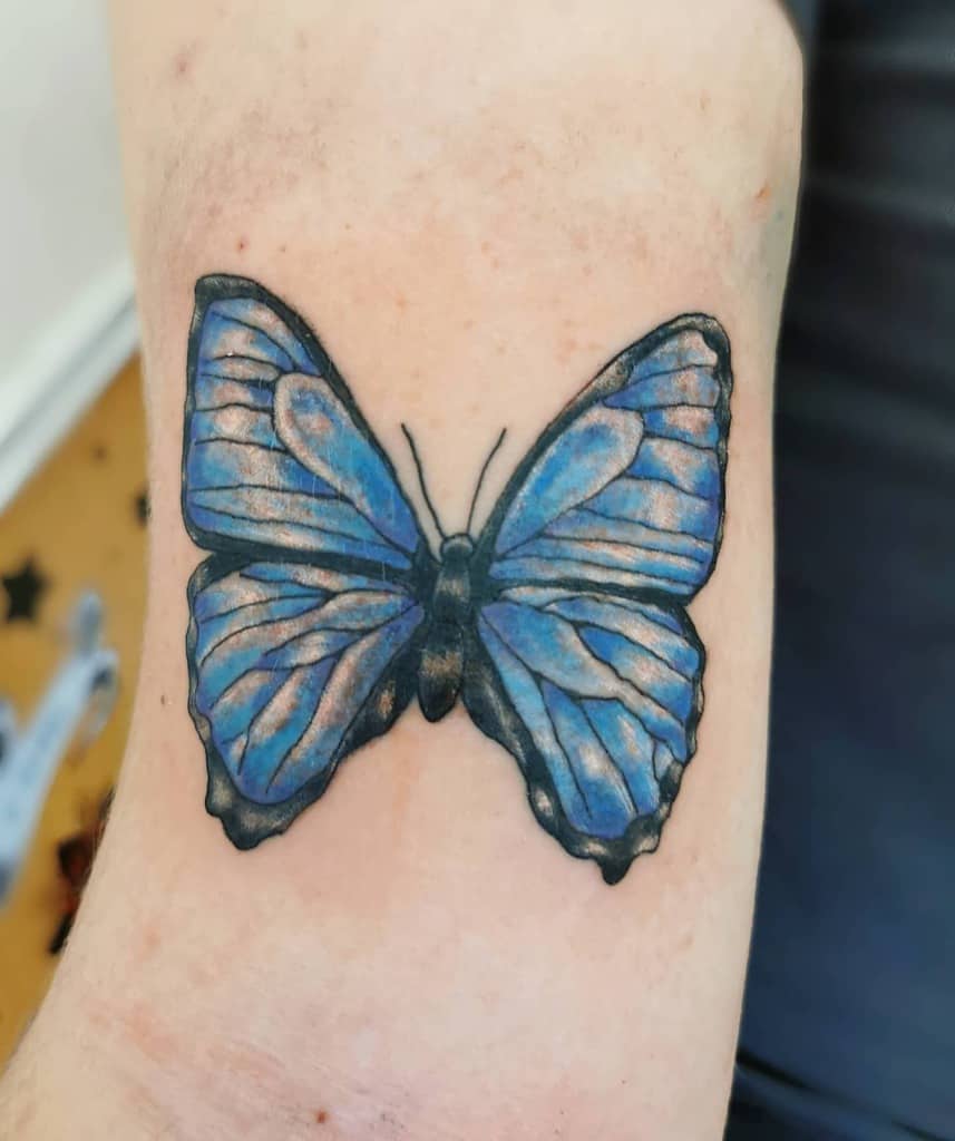 A vivid blue butterfly with striking black outlines graces the person's skin as a beautiful tattoo
