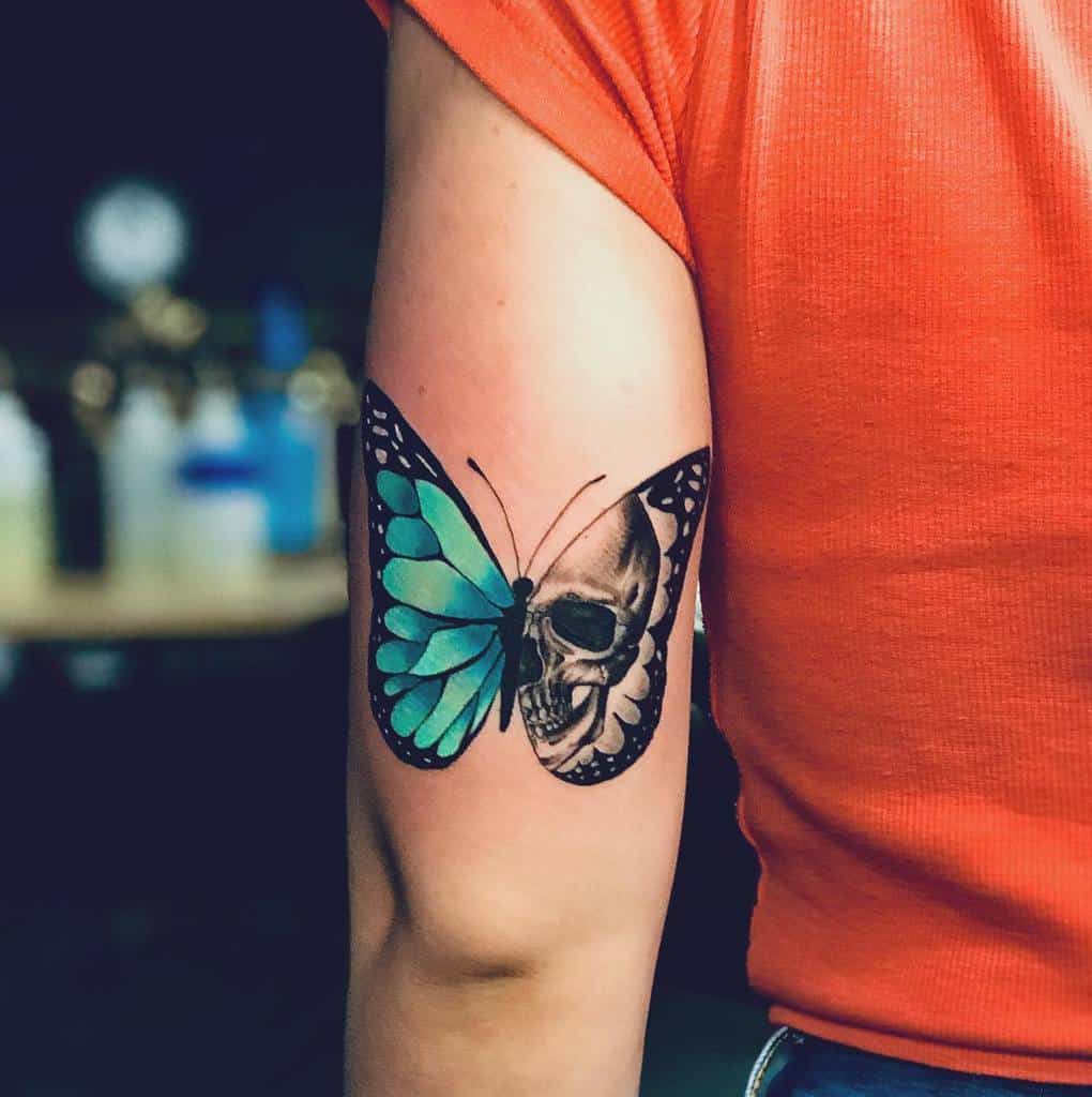 A tattoo of a blue butterfly with one wing and a skull on the other on an upper arm