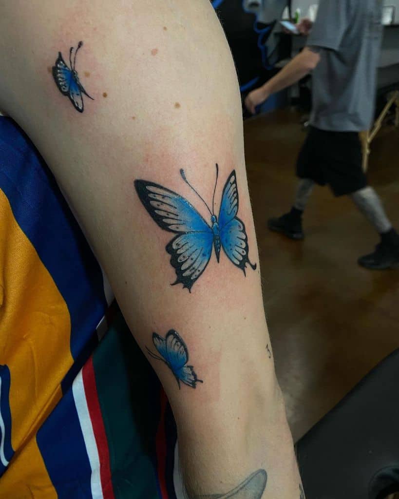 Arm adorned with intricate blue butterfly tattoos, featuring one large and two small butterflies