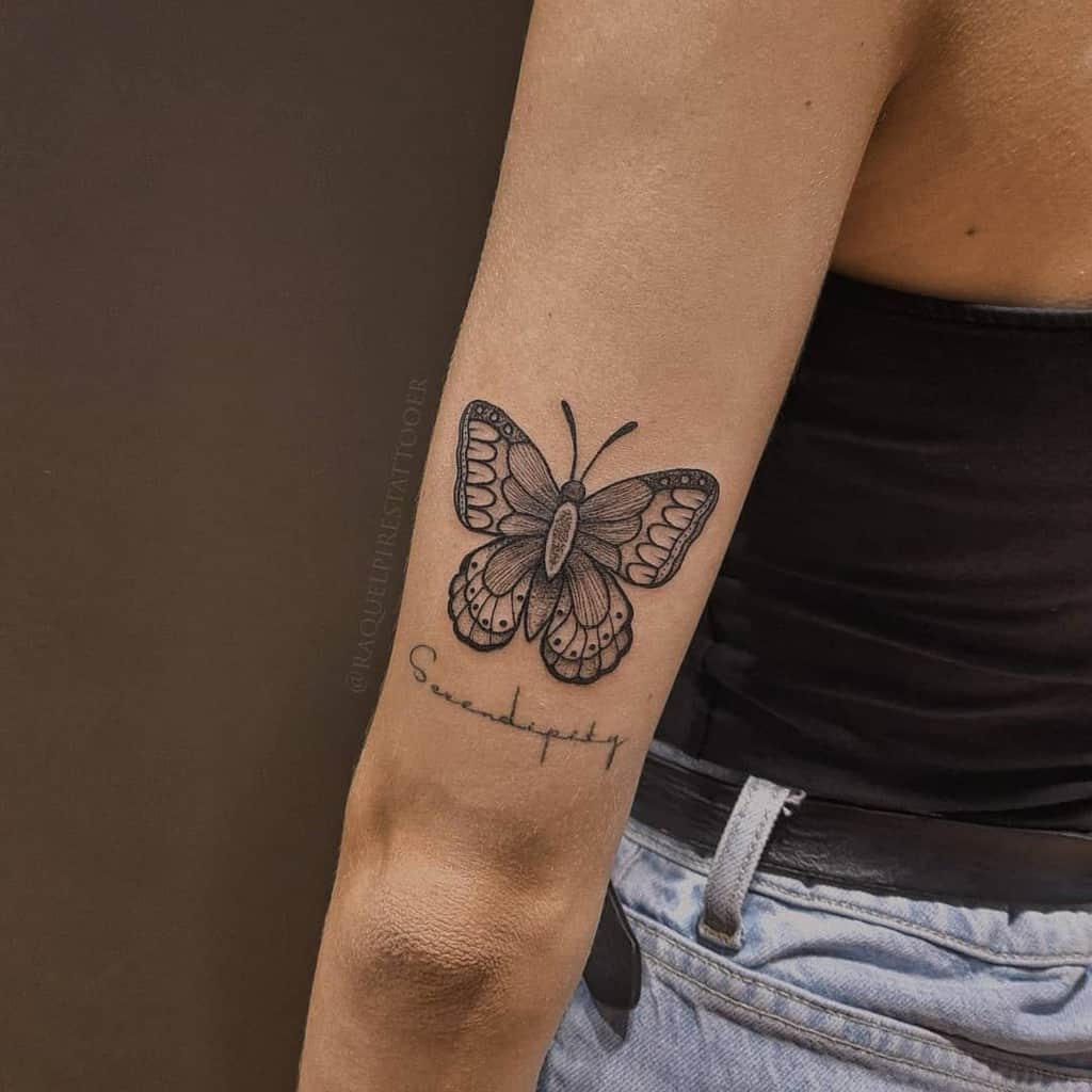 Black and white butterfly tattoo with cursive text below on a person's upper arm