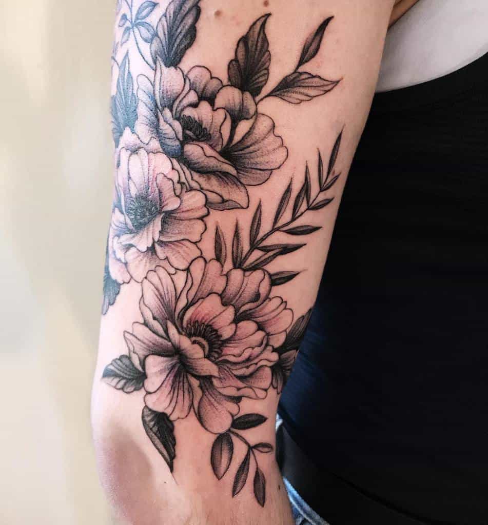 A stunning floral sleeve tattoo winds gracefully around the arm, with leaves intricately detailed in black ink
