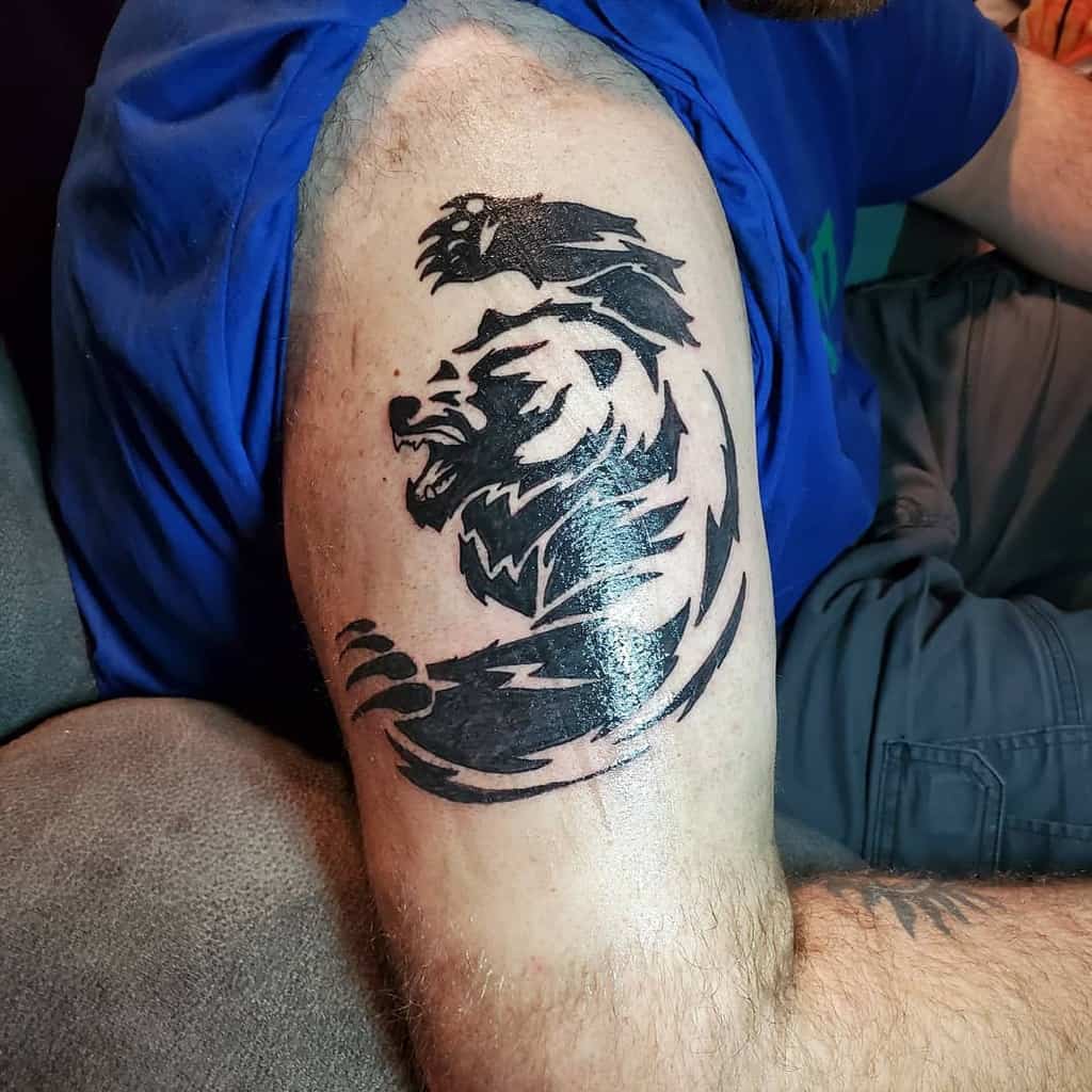 A striking bear tattoo design adorns a person's bicep, featuring bold black lines and dynamic styling that captures the creature’s power