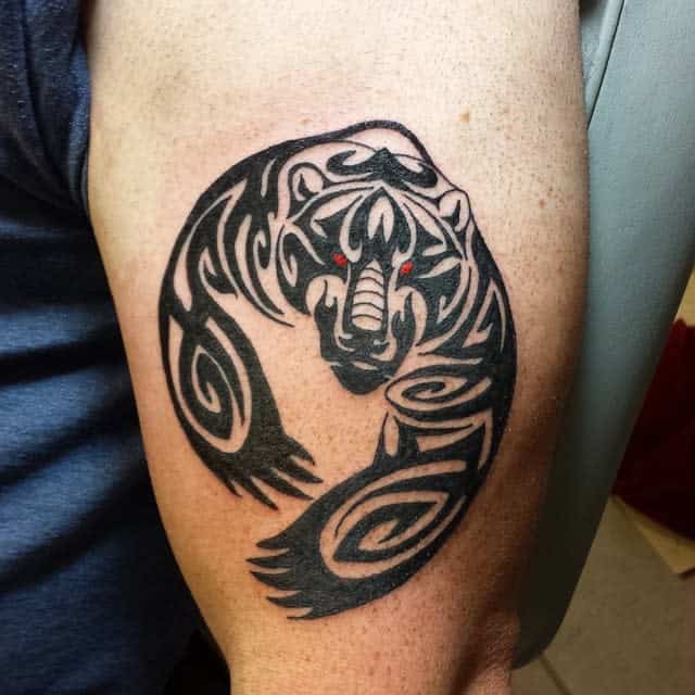 Arm tattoo of a tribal design showcasing a menacing bear with striking red eyes, capturing its raw power and spirit