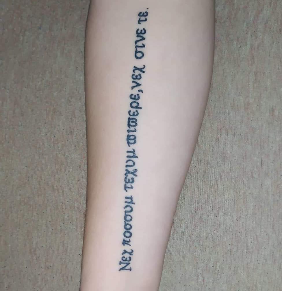 A forearm tattoo featuring a vertical line of text in a stylized script, resembling the writing style associated with the character Uta from Tokyo Ghoul