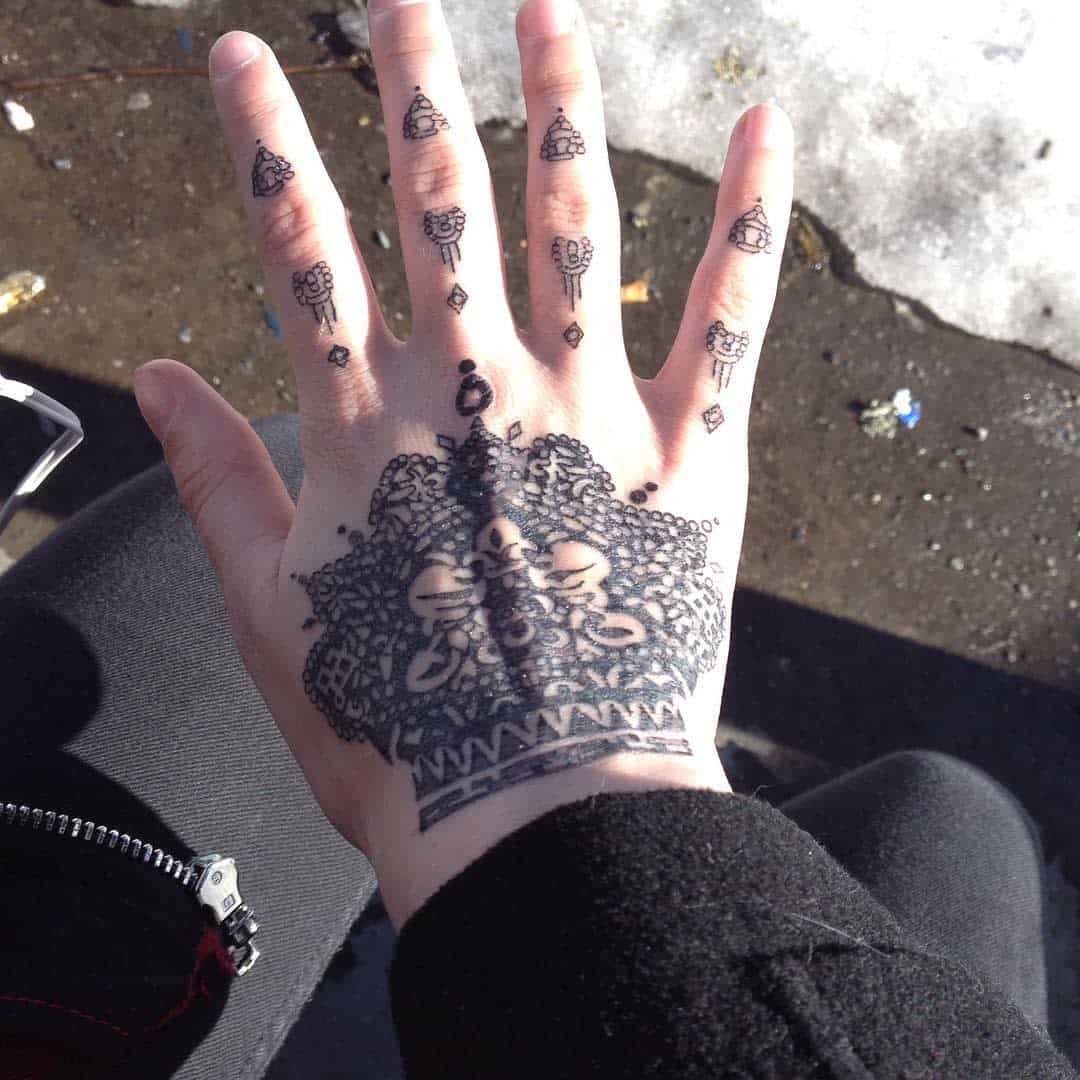Black intricate hand tattoo inspired by Uta from Tokyo Ghoul, featuring detailed geometric and floral patterns extending from the fingers to the back of the hand, with small, symmetrical designs on each finger
