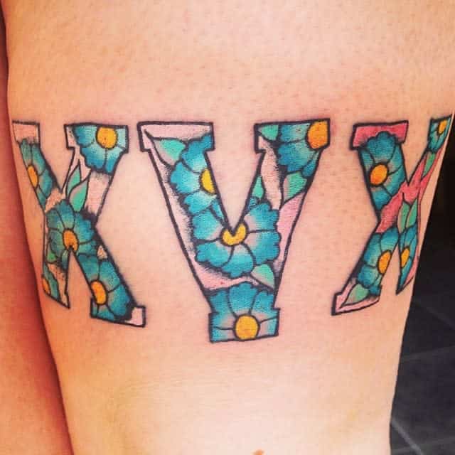 Straight edge tattoo of the letters "XVX" filled with blue flowers and green leaves