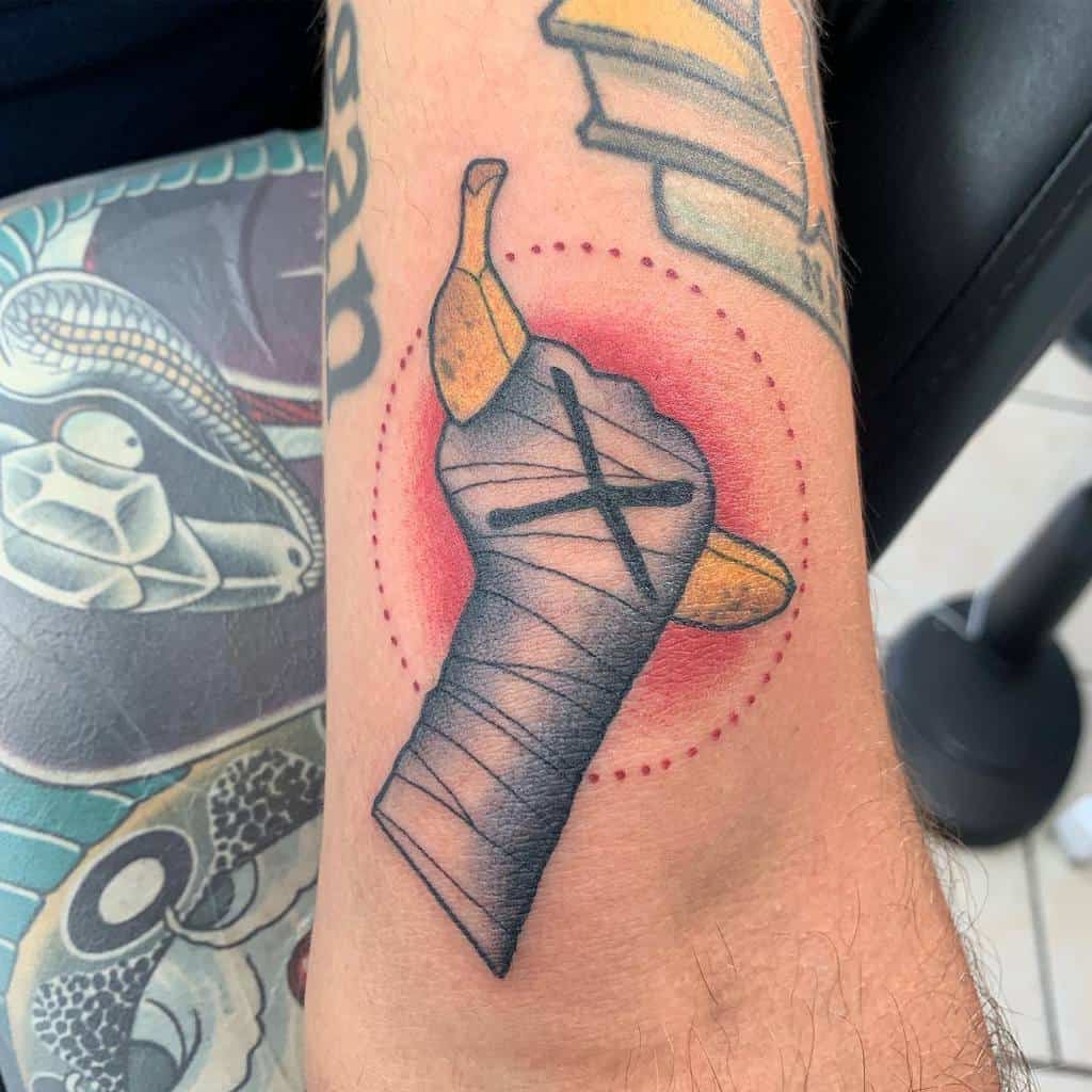 Straight edge tattoo of a hand with wrist wraps holding a banana, encircled by a dotted line and red background
