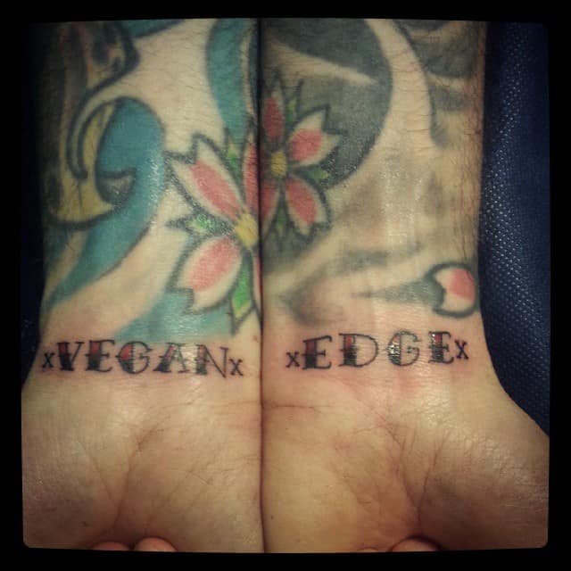 Two wrists with "xVEGANx" and "xEDGEx" straight edge tattoos in bold font, background features colorful floral and abstract tattoos