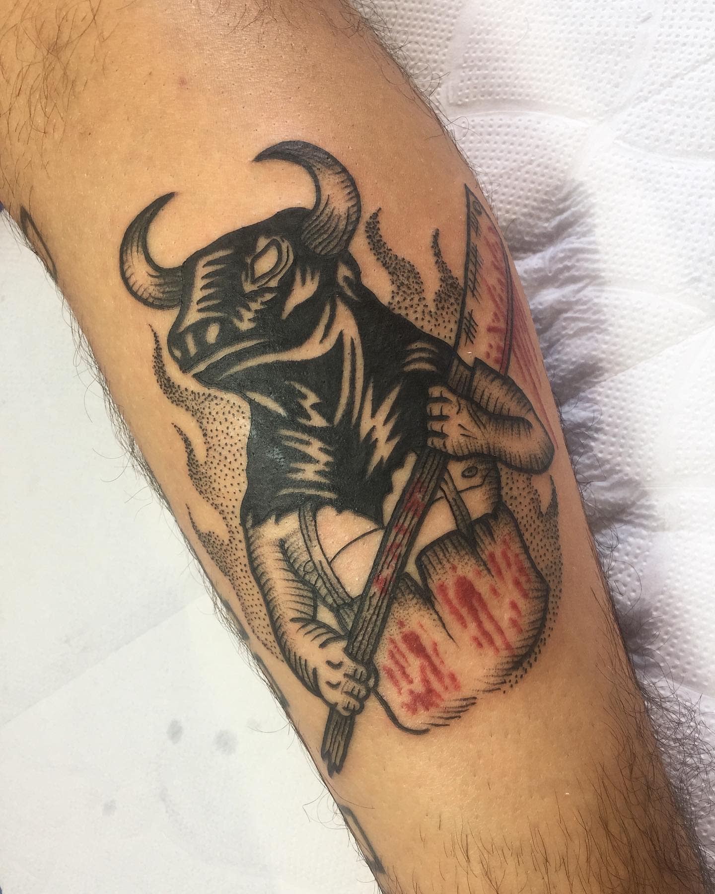 Tattoo of a bull holding a bloody knife and axe on an arm