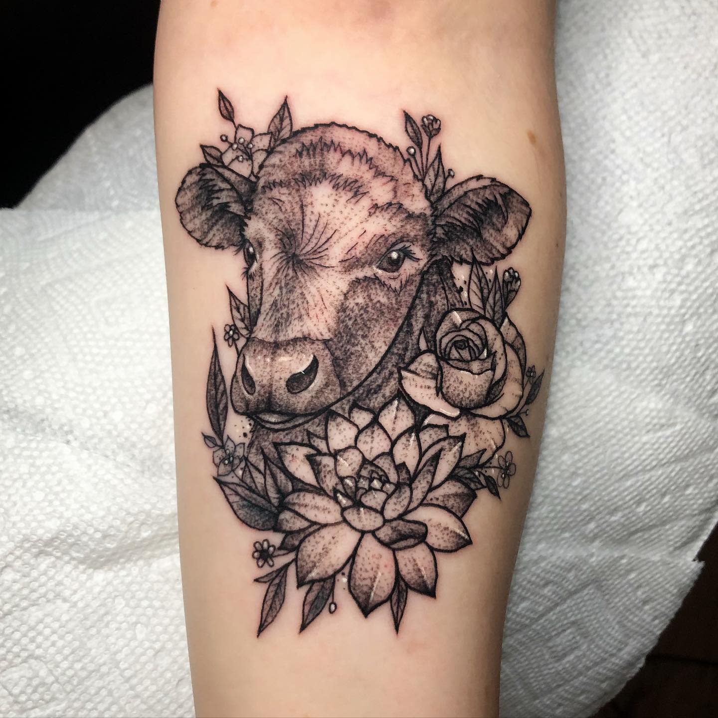 Tattoo of a cow's head surrounded by flowers on an arm