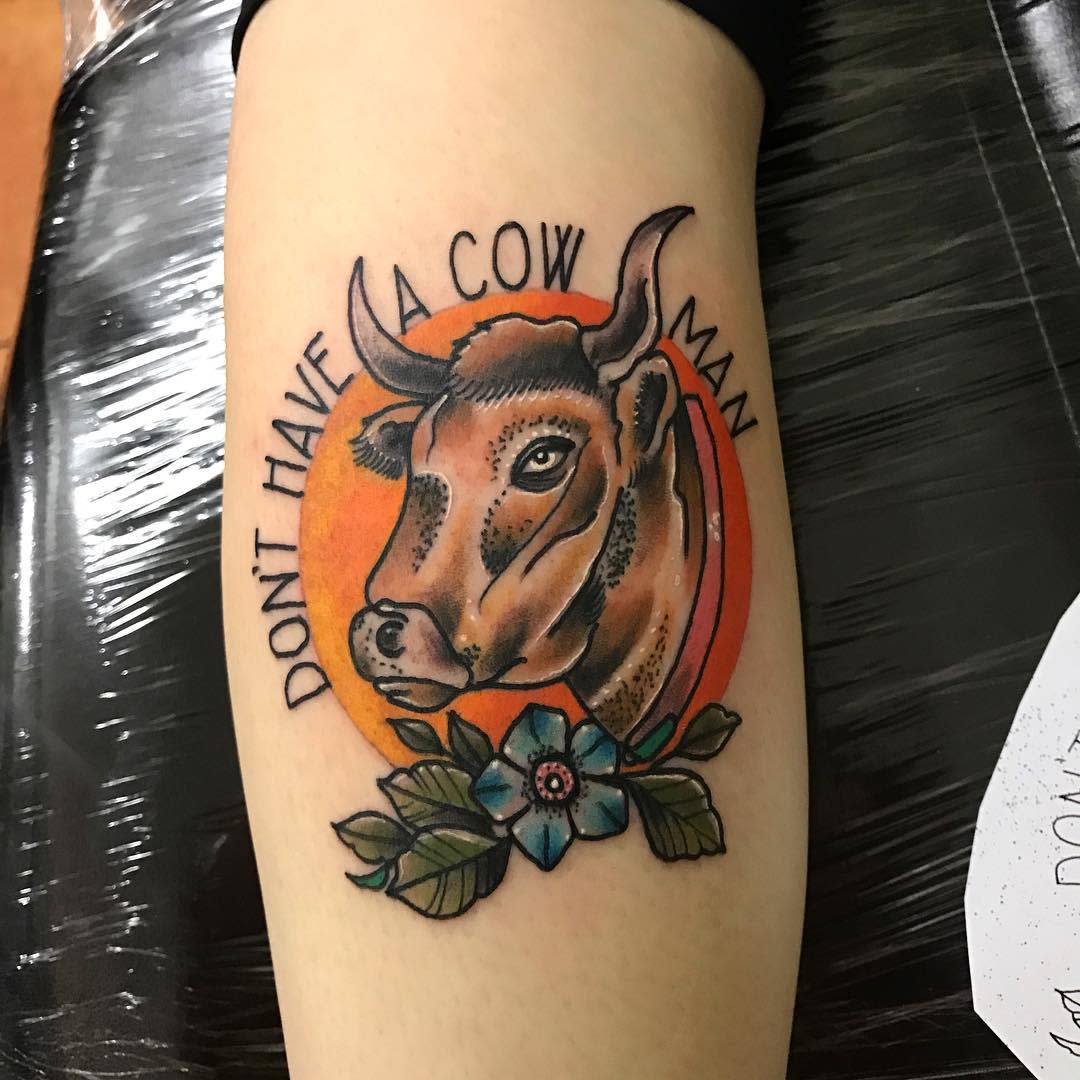 Tattoo of a cow inside an orange circle with text "Don't have a cow man" and a blue flower