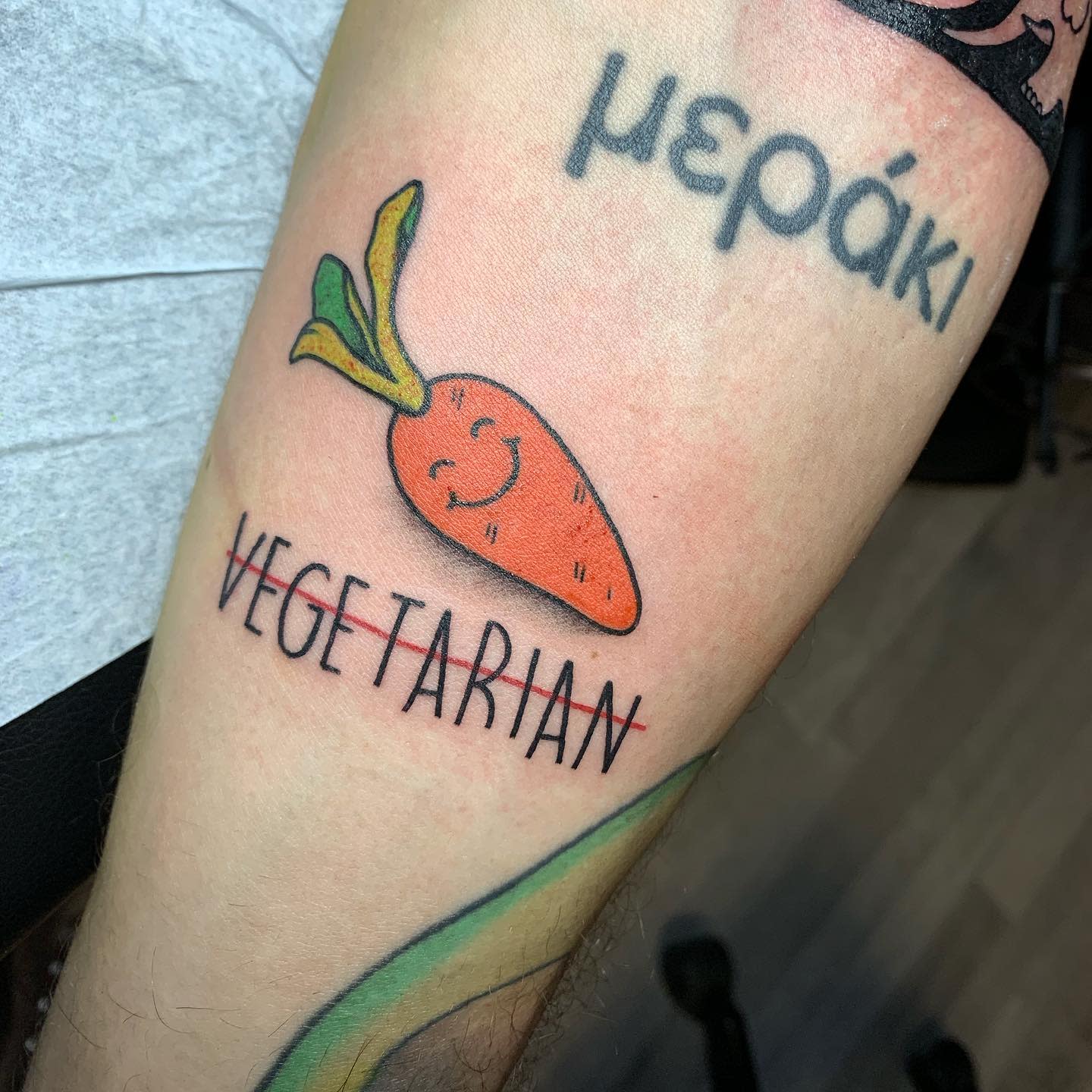 Tattoo of a smiling carrot with the word "VEGETARIAN" underneath it on an arm