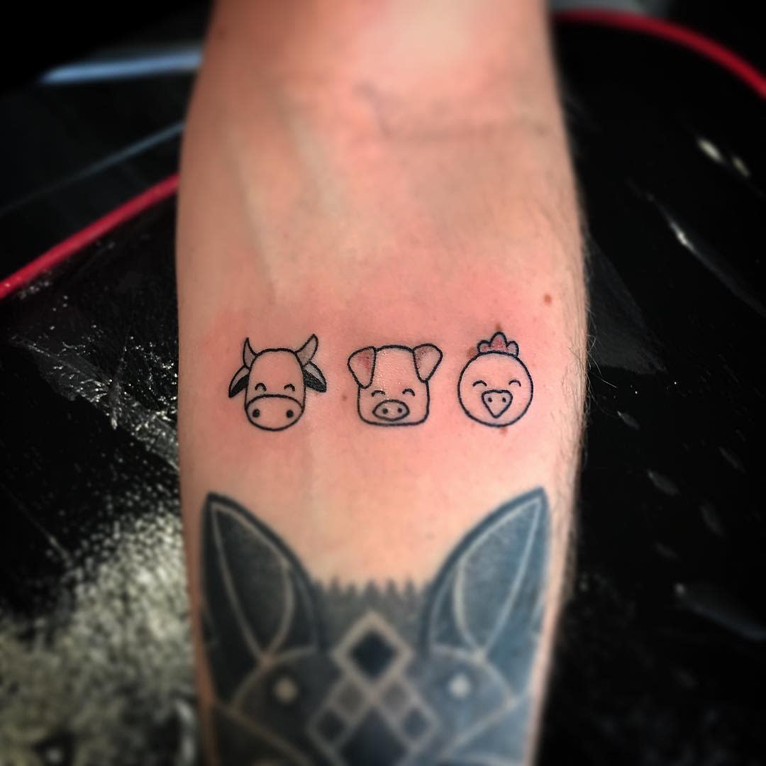 Three minimalist outline tattoos of a cow, pig, and chicken on a forearm