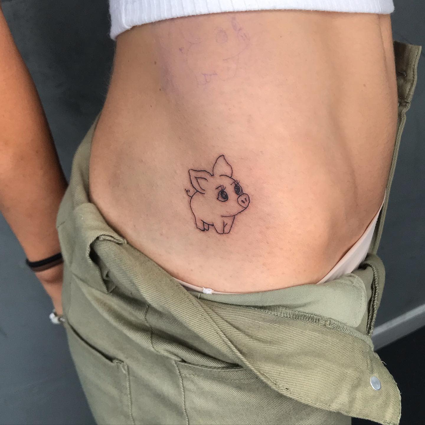 Simple line-art tattoo of a small piglet on a side above the waistband