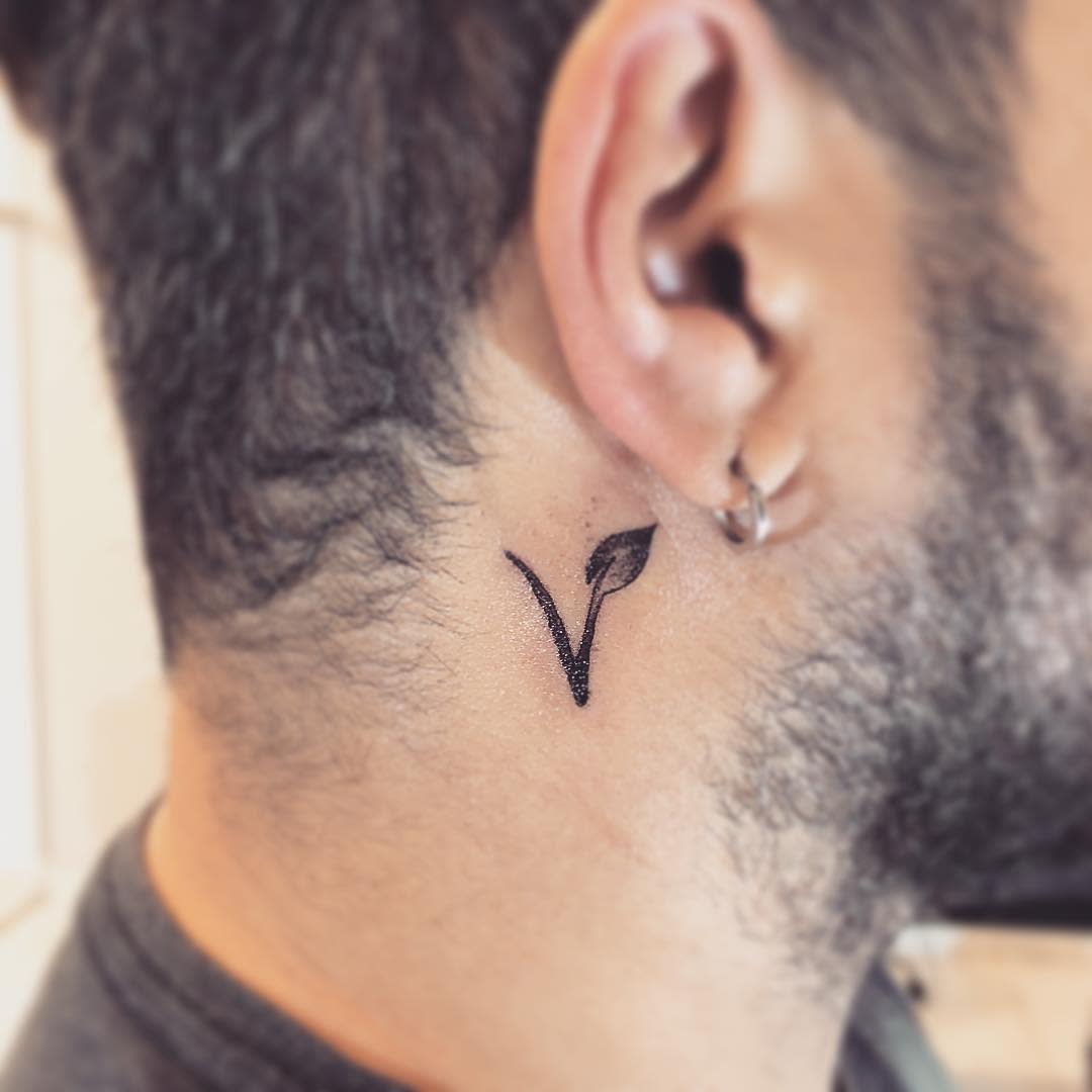 Small "V" tattoo with a leaf on the neck behind the ear