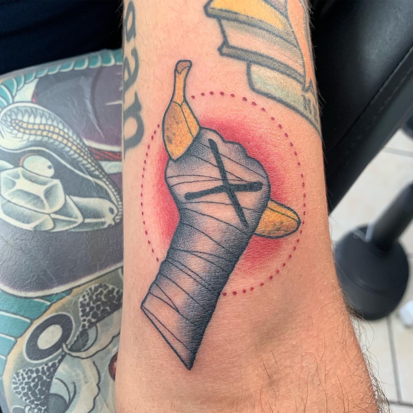 Tattoo of a bandaged hand holding a peeled banana with a dotted red circle background