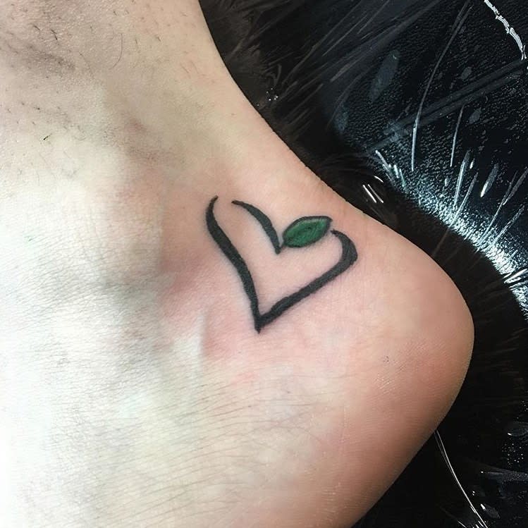 Tattoo of an abstract heart with a green leaf at its top, located on an ankle