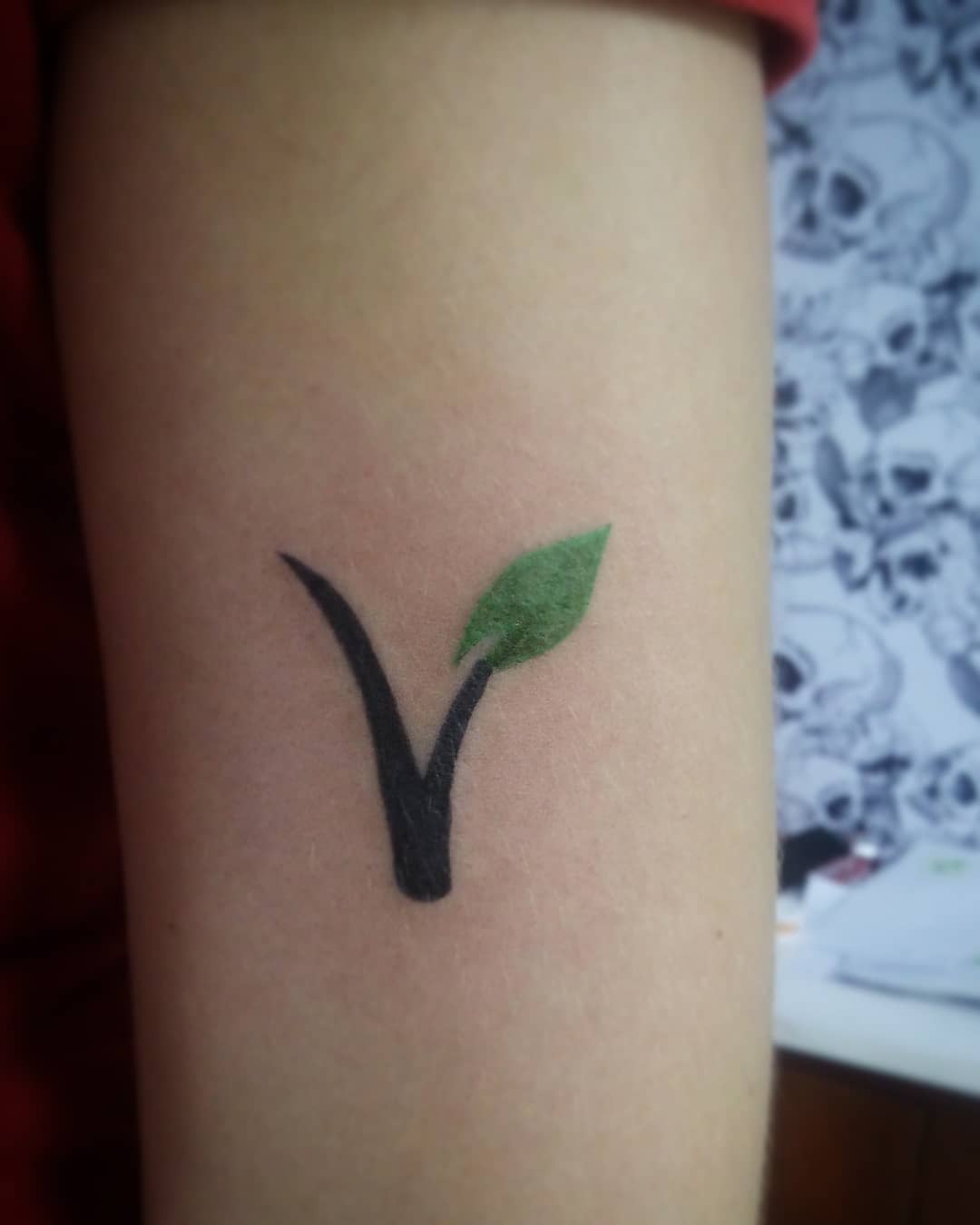 Tattoo of a black 'V' with a green leaf on an arm