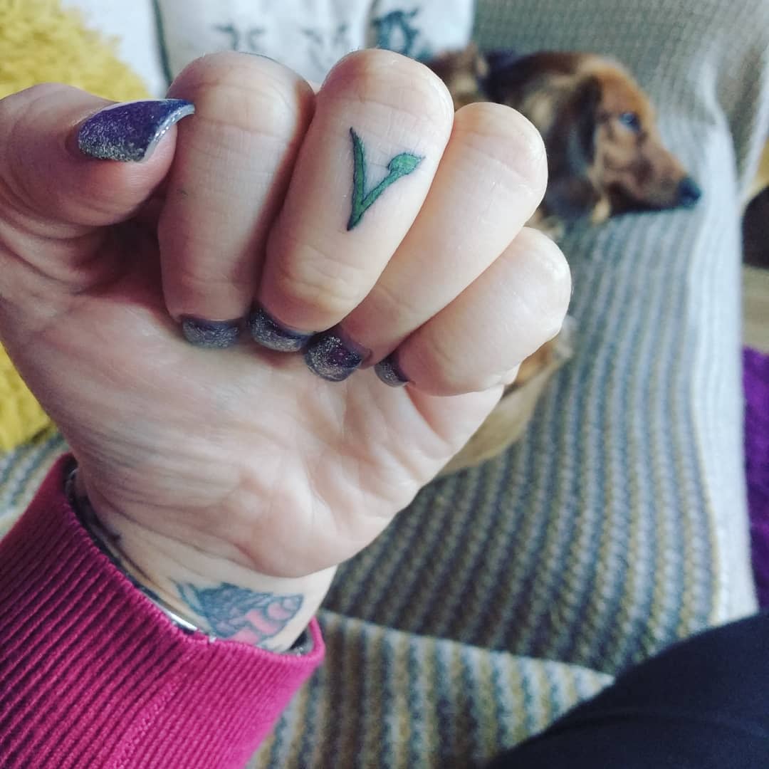 Close-up of a fist showing a small "V" tattoo on a finger