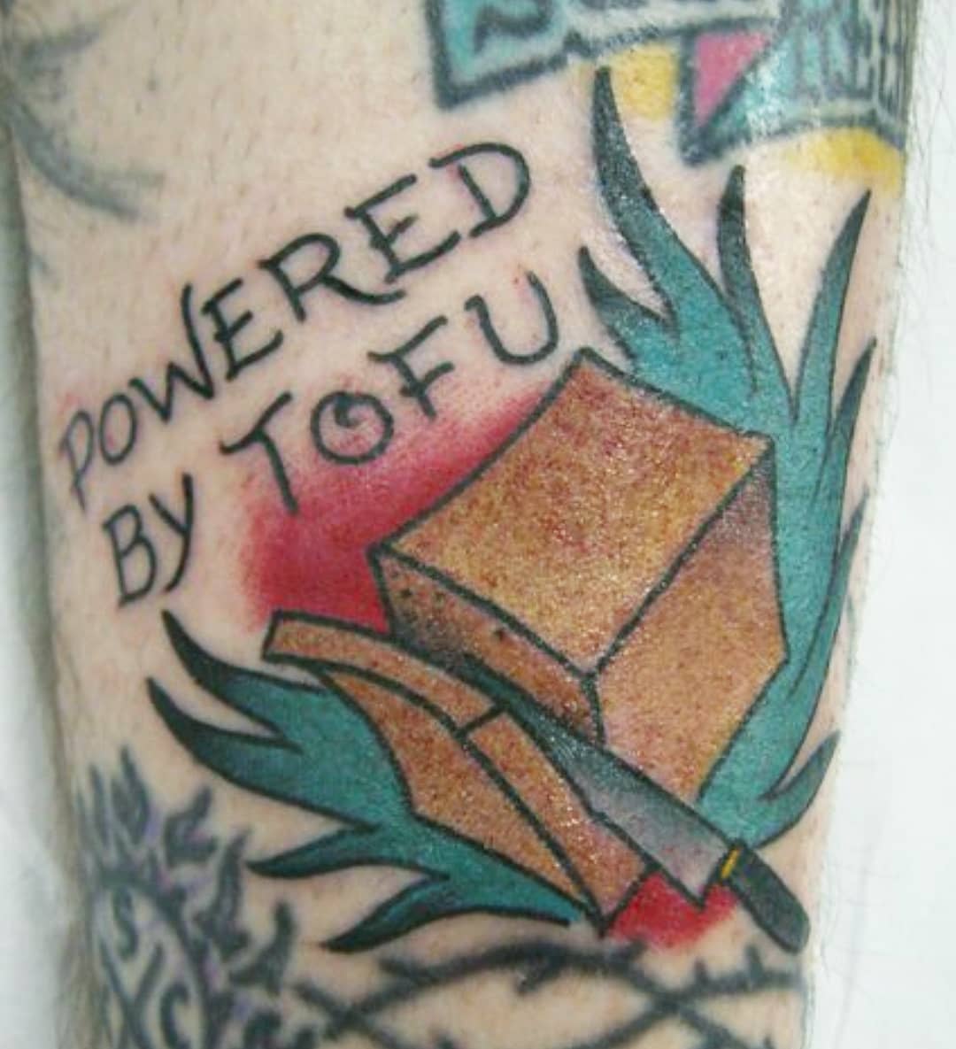 Tattoo with "Powered by Tofu" text, depicting tofu with leaves and a knife