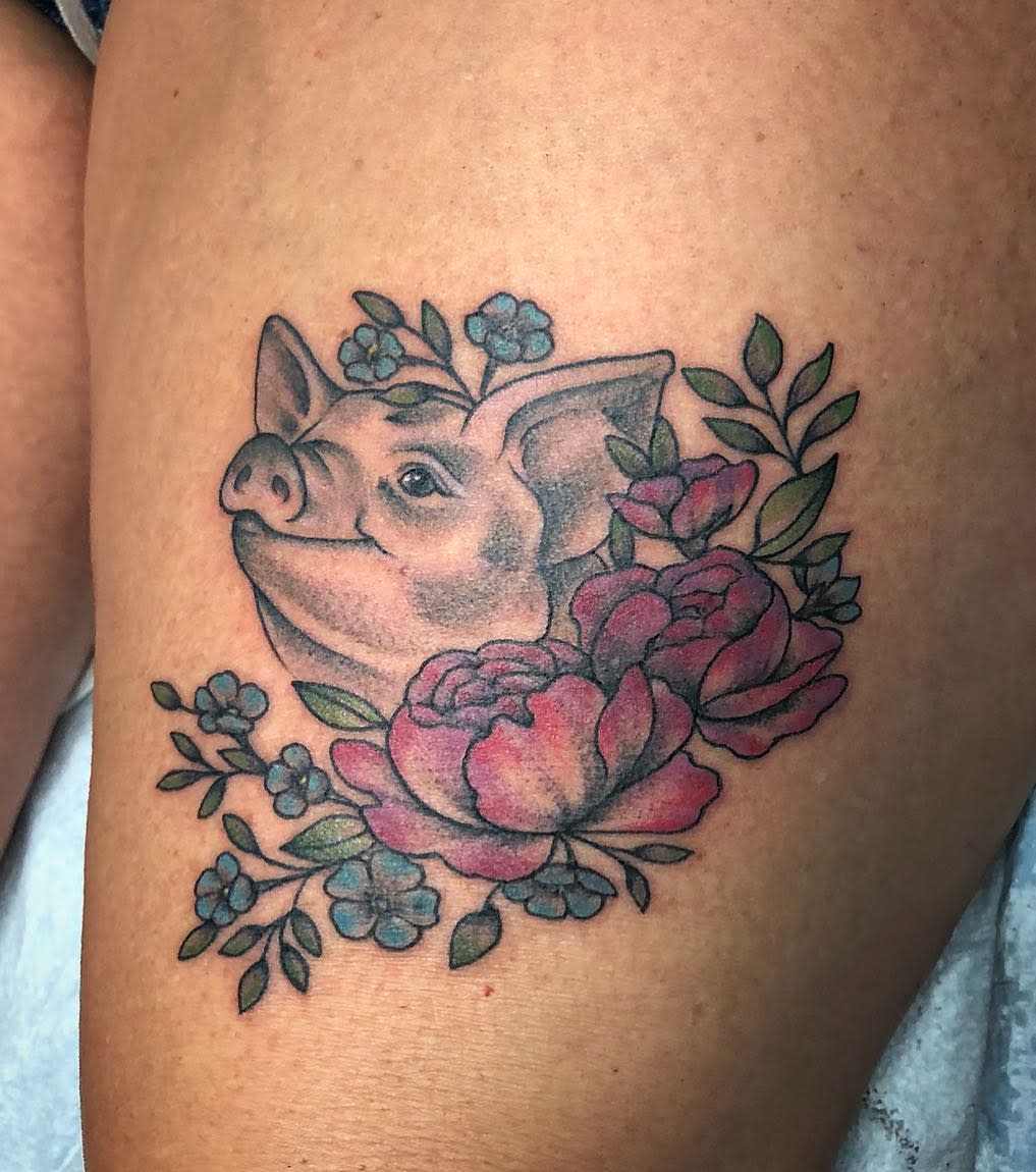 Tattoo of a pig with floral accents, including roses and blue flowers, on skin