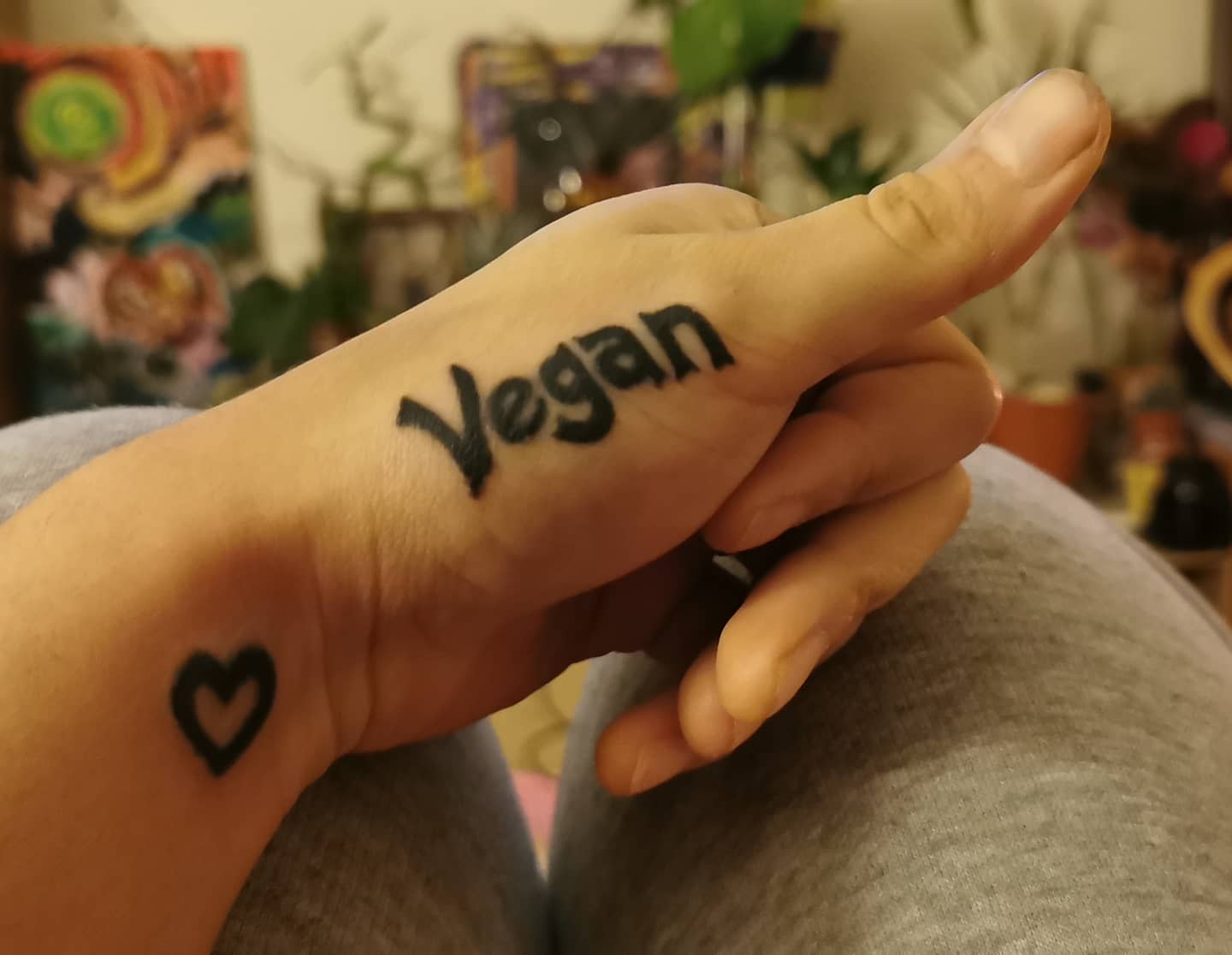 Hand with "Vegan" tattoo on thumb and heart tattoo on wrist