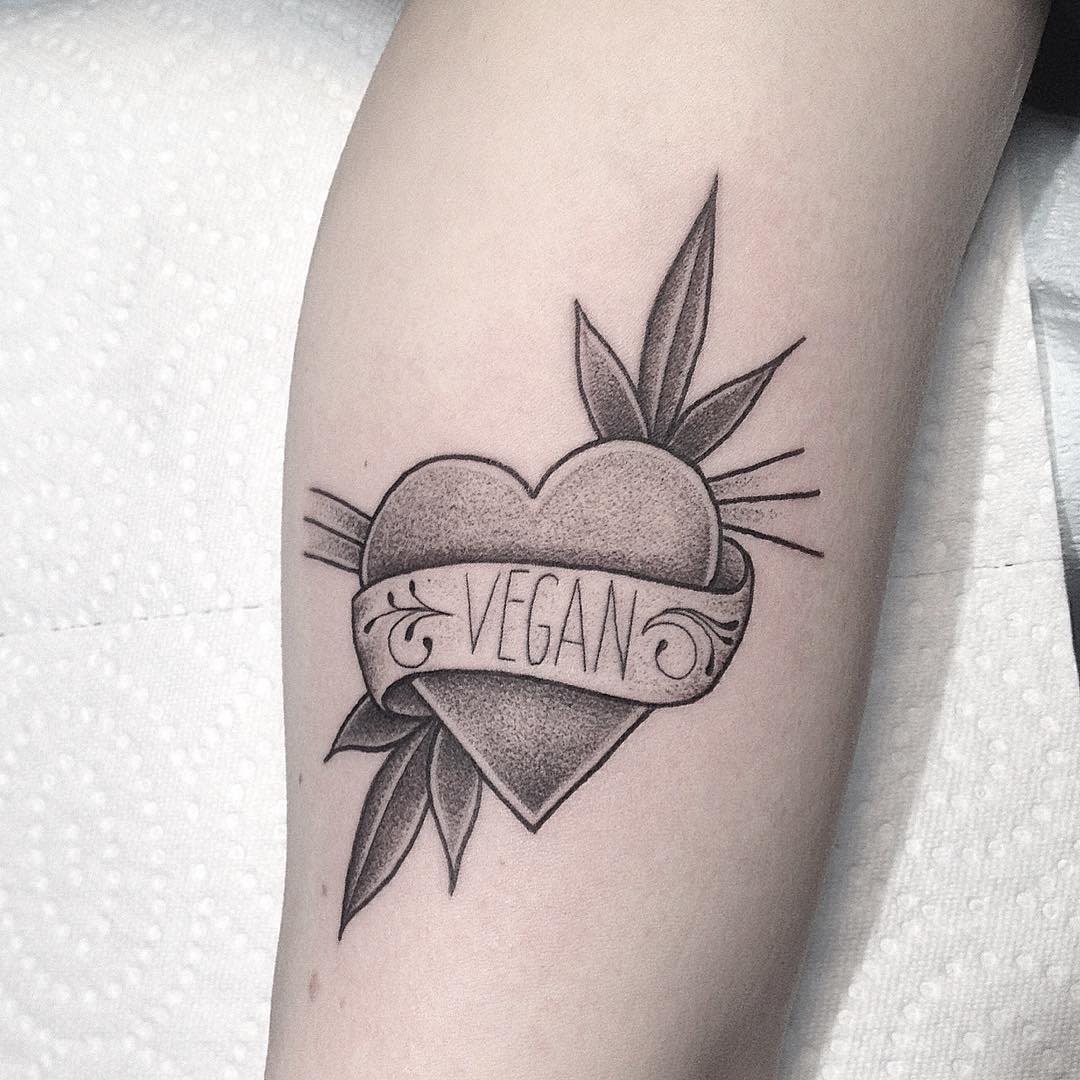 Heart-shaped tattoo with the word "Vegan" on a banner, surrounded by leaves