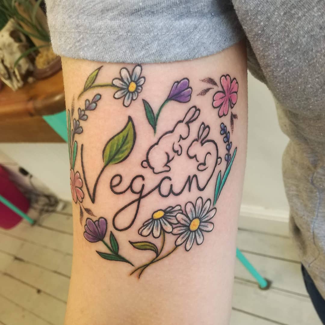 Tattoo featuring the word "Vegan", surrounded by flowers and two bunny silhouettes
