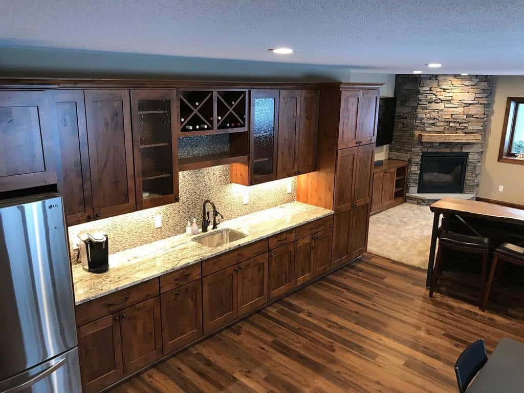 Rustic wood kitchen with granite countertops, wine storage, and stone fireplace in the background.