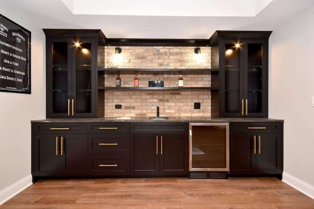 Sleek modern basement bar with black cabinets, brick backsplash, and gold hardware accents.