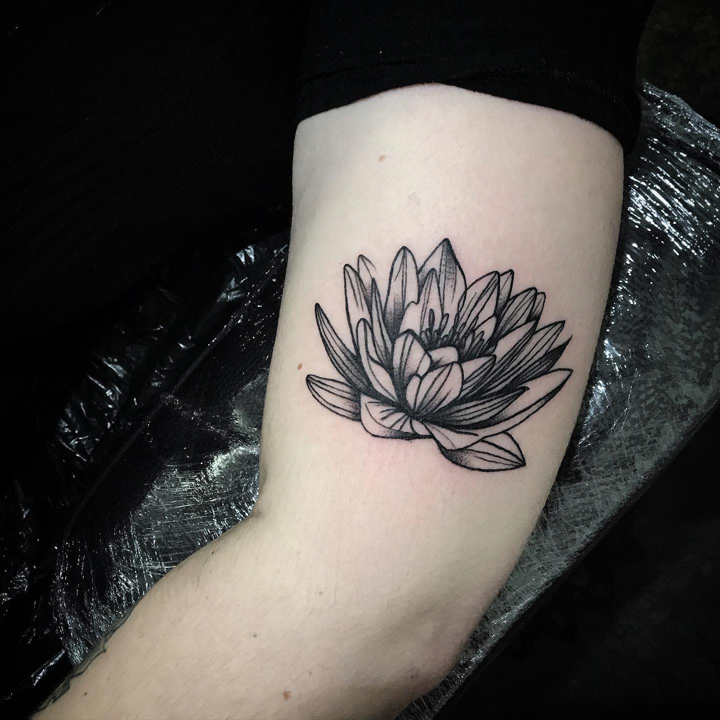 A simple black ink water lily tattoo on the inner arm, featuring clean lines and minimal shading