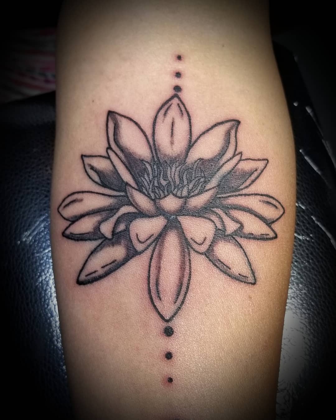 A simple black ink water lily tattoo with dot accents above and below, located on the forearm