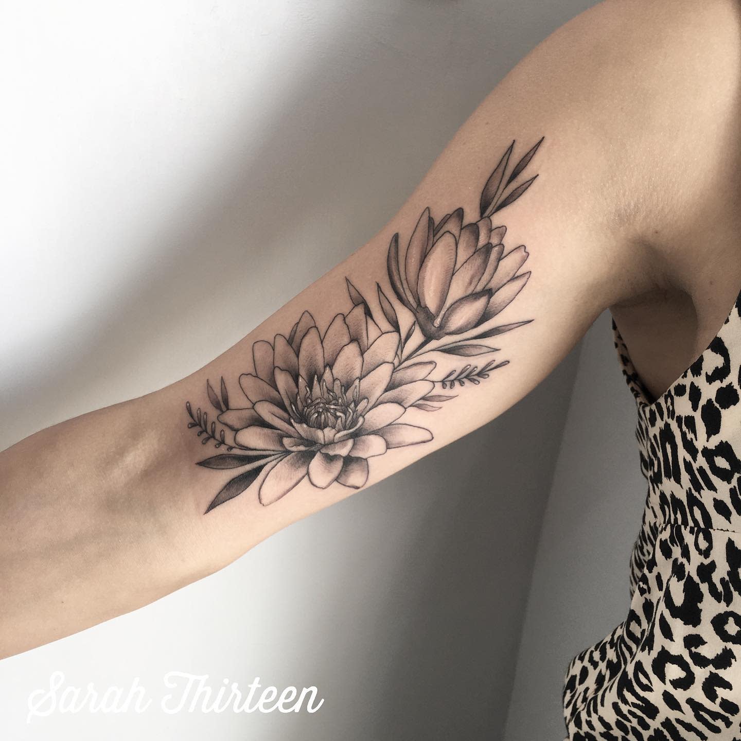 A delicate black and grey water lily tattoo on the inner arm, featuring two flowers and leafy accents