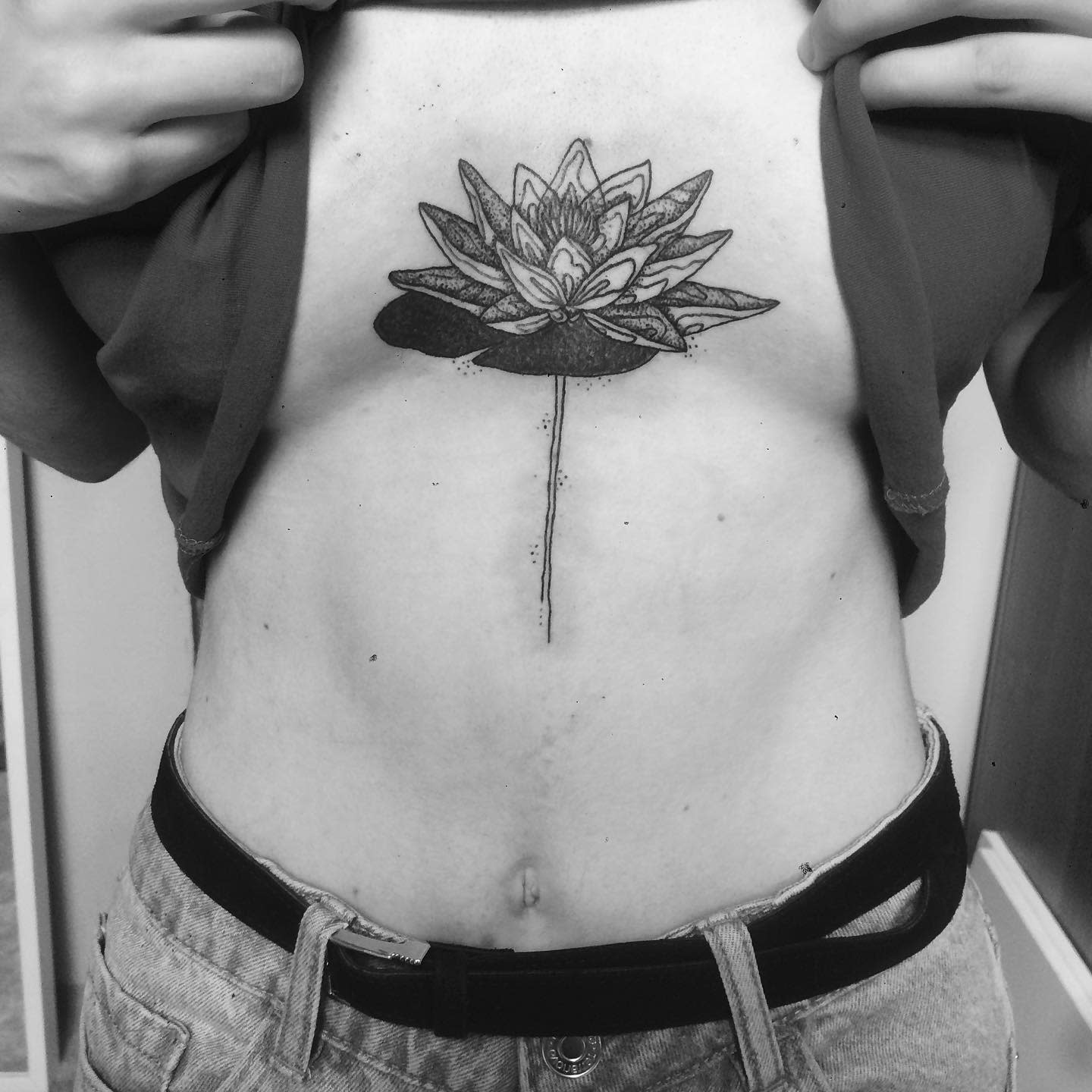 A minimalistic black ink water lily tattoo on the sternum, featuring detailed petals and a long stem extending downward