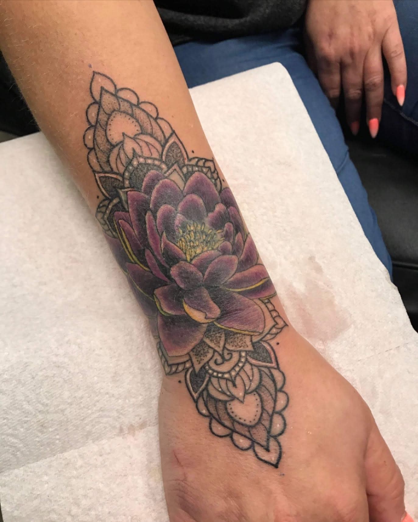 A detailed purple water lily tattoo on the forearm, incorporating intricate mandala designs that extend toward the wrist and hand
