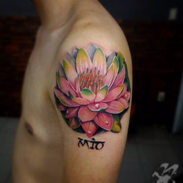 A realistic water lily tattoo on the upper arm, featuring pink and green petals with water droplets, and a small script tattoo below the flower