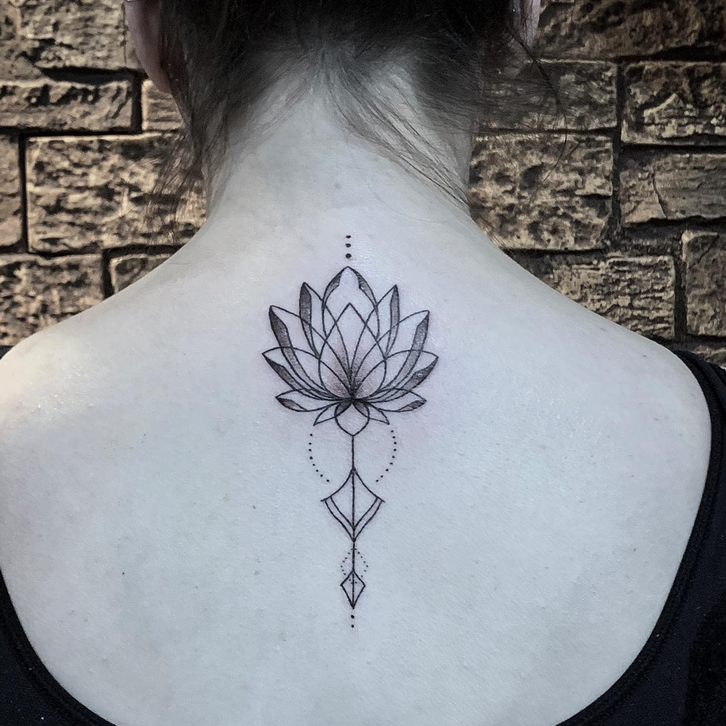 A minimalist geometric water lily tattoo on the upper back, featuring clean lines, dot work, and abstract shapes extending downward, creating an elegant and symmetrical design