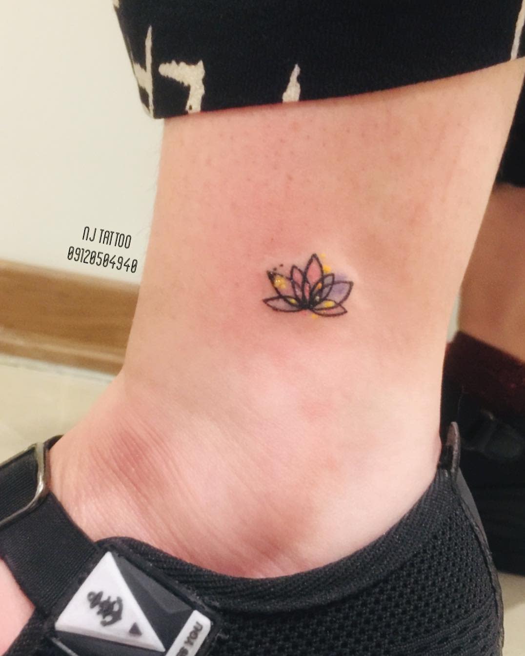 A tiny, colorful water lily tattoo on the ankle, featuring delicate petals in shades of pink, purple, and yellow with fine black outlines