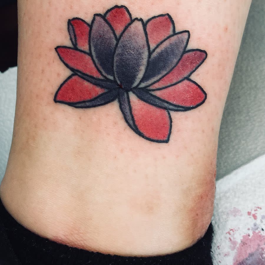 A small traditional-style water lily tattoo on the ankle, featuring bold red and black petals with simple shading and thick black outlines