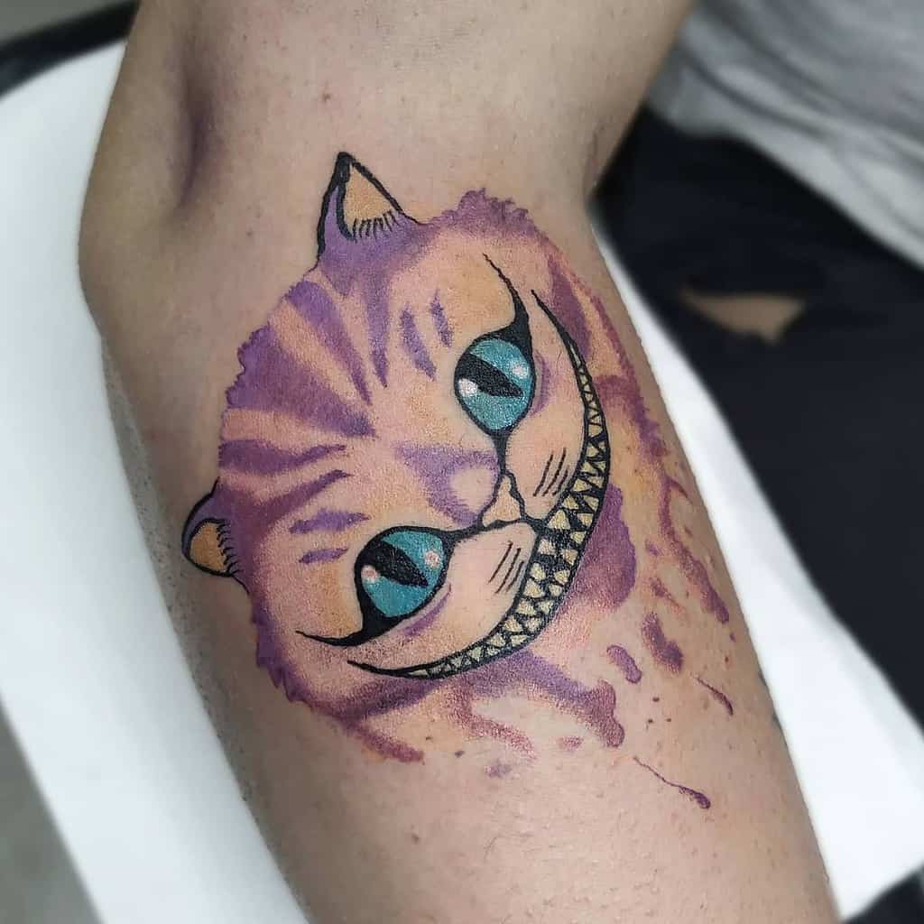 Tattoo of a grinning purple and pink Cheshire cat with blue eyes on a person's arm