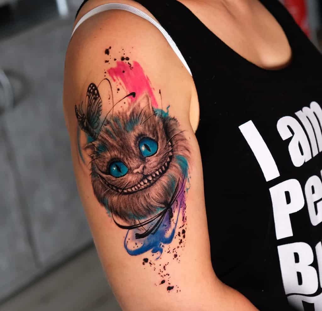 Colorful Cheshire Cat tattoo with a butterfly on a person's upper arm