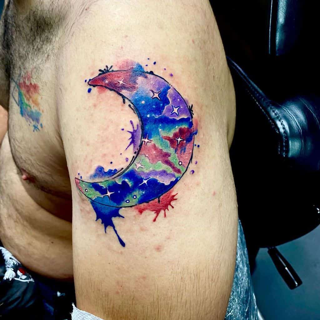 Colorful crescent moon tattoo with abstract splashes on upper arm