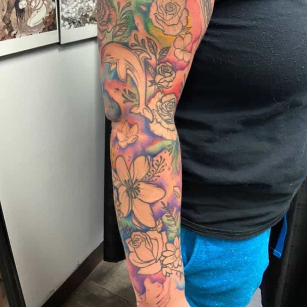 A vibrant sleeve of tattoos wraps around the arm, showcasing colorful flowers intertwined with a playful dolphin design