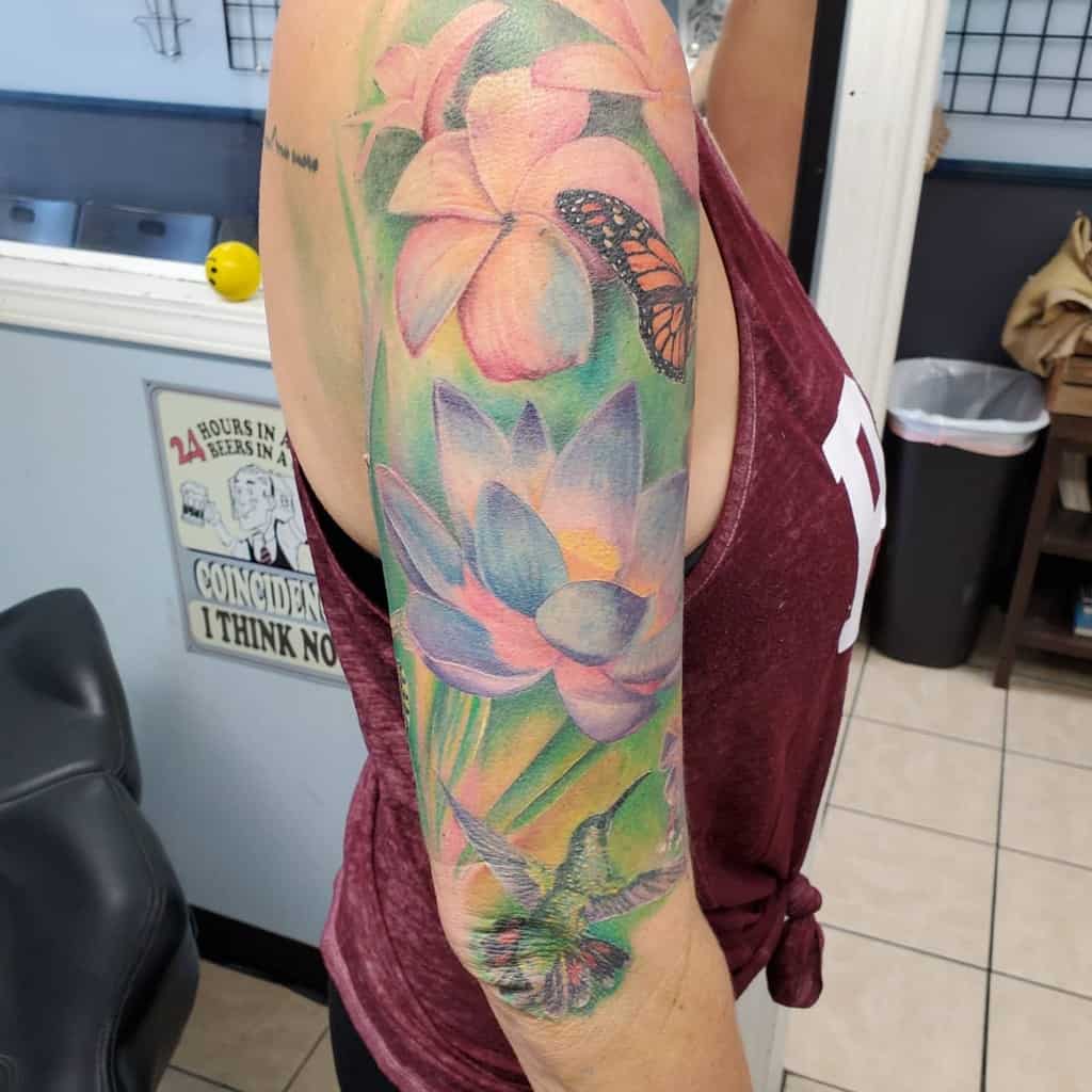 A vibrant sleeve tattoo showcasing colorful flowers, butterflies, and a hummingbird graces the upper arm