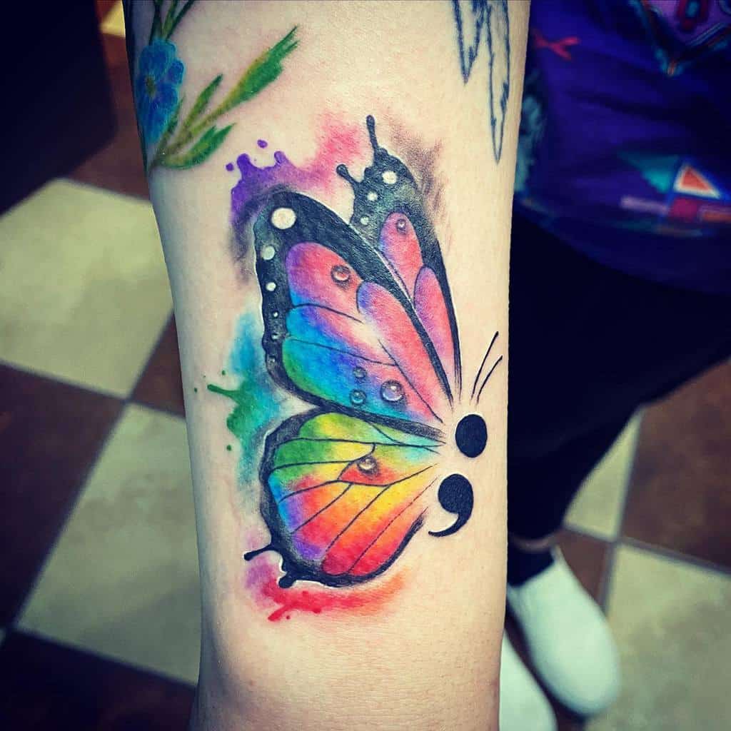 A vibrant watercolor butterfly tattoo with a semicolon body, symbolizing mental health struggles and resilience